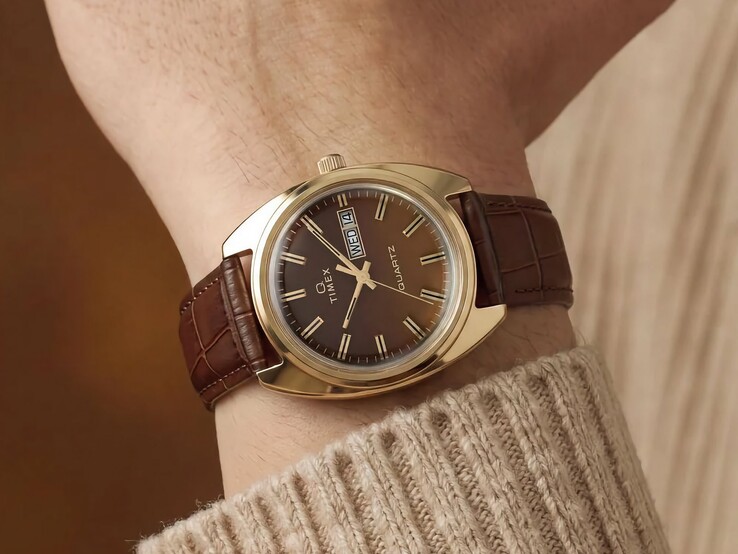 Timex Q 1976 Day and Date con esfera fumé marrón y caja en tono dorado, mostrado en una muñeca con una correa de cuero marrón.