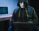 Una figura enmascarada y encapuchada trabaja con un ordenador portátil en una habitación a oscuras.