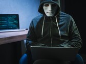 Una figura enmascarada y encapuchada trabaja con un ordenador portátil en una habitación a oscuras.