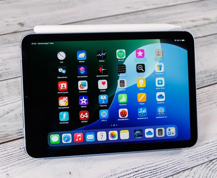 Vista frontal de un iPad mini con el Apple Pencil apoyado encima, mostrando la pantalla de inicio mientras está colocado sobre una superficie de madera. (Fuente de la imagen: Notebookcheck)