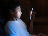Un adolescente en una habitación a oscuras mirando un smartphone iluminado