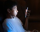Un adolescente en una habitación a oscuras mirando un smartphone iluminado
