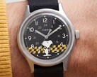 Primer plano de la esfera negra del Timex MK1, en la que aparece Snoopy sobre un fondo a cuadros amarillos y negros, con índices arábigos y agujas luminosas.
