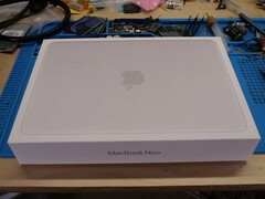 Caja de venta del MacBook Neo colocada en un banco de trabajo antes del desmontaje para la actualización de la SSD
