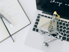 Carrito de la compra en miniatura sobre el teclado de un ordenador portátil, con el mensaje «Comprar ahora» en la pantalla