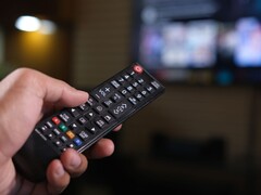 Mano sosteniendo un mando a distancia con un televisor desenfocado de fondo