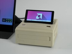Un mini PC Ayaneo AM01S de estilo retro en acabado beige, con una pantalla secundaria abatible integrada que muestra el escritorio de Windows. (ETA Prime vía YouTube)