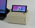 Un mini PC Ayaneo AM01S de estilo retro en acabado beige, con una pantalla secundaria abatible integrada que muestra el escritorio de Windows. (ETA Prime vía YouTube)