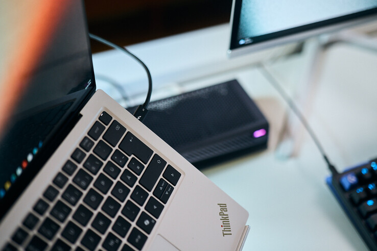 Primer plano de un cable Thunderbolt 5 conectado al puerto lateral de un portátil Lenovo ThinkPad X9, con la eGPU Aorus al fondo.