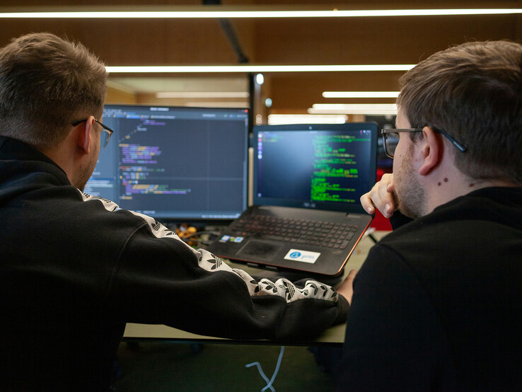 Investigadores analizando código en monitores duales (Fuente de la imagen: Flipsnack / Unsplash)