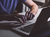 Unas manos tecleando en el teclado de un MacBook con poca luz, con el logotipo de Apple iluminado.