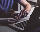 Unas manos tecleando en el teclado de un MacBook con poca luz, con el logotipo de Apple iluminado.
