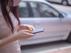 Una mujer escribiendo en su smartphone con un coche plateado al fondo