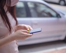 Una mujer escribiendo en su smartphone con un coche plateado al fondo