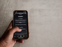 Mano sosteniendo un smartphone que muestra la interfaz de ChatGPT sobre una superficie de piedra gris