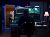 Un investigador encapuchado trabaja en varias pantallas en un montaje a oscuras. En la foto, un hacker genérico.