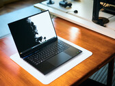 Un portátil para juegos Razer Blade 16 de color negro mate, con la tapa abierta, colocado sobre una alfombrilla de escritorio blanca que recubre una mesa de madera de tonos cálidos, en el que se muestra un fondo de pantalla en blanco y negro de gran intensidad.