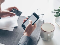 Persona que teclea en un smartphone mientras sostiene una tarjeta bancaria en la otra mano