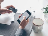 Persona que teclea en un smartphone mientras sostiene una tarjeta bancaria en la otra mano