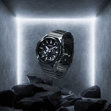 G-Shock GST-B1000BD-1A suspendido sobre rocas oscuras en un espacio de exposición de hormigón, resaltando su construcción de acero inoxidable negro.