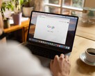 Persona frente a una computadora portátil con la página principal de Google abierta, junto a una taza de café