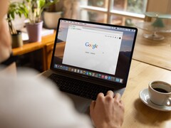 Persona frente a una computadora portátil con la página principal de Google abierta, junto a una taza de café
