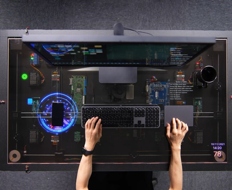 El escritorio de HTX Studio, inspirado en AirPower y de montaje propio, en uso, con un teléfono cargándose en la pantalla transparente junto al teclado, el trackpad y el monitor.