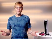  Mark Cerny durante un evento de PlayStation, sentado junto a una consola PS5 y los mandos DualSense. (Fuente de la imagen: Sony Interactive Entertainment)