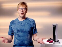 Mark Cerny durante un evento de PlayStation, sentado junto a una consola PS5 y los mandos DualSense. (Fuente de la imagen: Sony Interactive Entertainment)