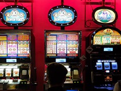 Máquinas tragaperras en el interior de un casino con pantallas luminosas y gente jugando delante (Fuente de la imagen: djedj via Pixabay)