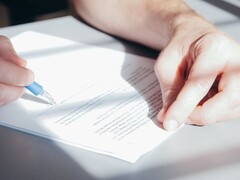 Una mano firma un documento con un bolígrafo azul.