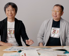 Una captura de pantalla de Shigru Miyamoto y Tezuka Takashi con camisetas del 30º aniversario de Super Mario Bros