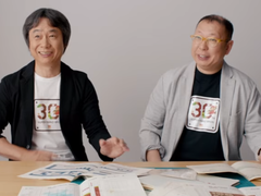 Una captura de pantalla de Shigru Miyamoto y Tezuka Takashi con camisetas del 30º aniversario de Super Mario Bros