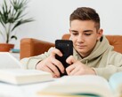 Un adolescente con sudadera con capucha escribiendo en un smartphone con los libros de clase abiertos delante de él