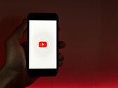 Una mano que sostiene un smartphone con el logotipo de YouTube iluminado en la pantalla sobre un fondo rojo