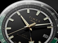 Primer plano de la esfera negra del Timex Atelier GMT Première M1a, con manecillas en tono dorado, índices horarios luminiscentes, ventana de fecha y anillo GMT de 24 horas en negro y verde.