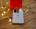 Un OnePlus 15 descansa sobre una mesa de madera rodeado de cálidas guirnaldas de luces, con una caja de venta al público de OnePlus de color rojo brillante situada al fondo.