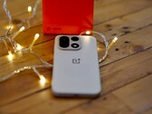 Un OnePlus 15 descansa sobre una mesa de madera rodeado de cálidas guirnaldas de luces, con una caja de venta al público de OnePlus de color rojo brillante situada al fondo.
