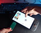 Yu del canal de YouTube Better Gaming sosteniendo una Nintendo Switch 2 en una mano y un adaptador PCB verde de código abierto en la otra, intentando insertarlo en la ranura microSD Express del dispositivo (Fuente de la imagen: Better Gaming vía YouTube)