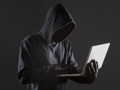 Un hacker encapuchado manejando un ordenador portátil sobre un fondo oscuro.