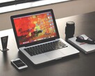 MacBook Pro sobre un escritorio oscuro junto a un teléfono inteligente, unas gafas y un cuaderno