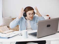 Hombre con auriculares levantando las manos con frustración frente a un portátil
