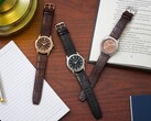 Tres relojes Citizen Rolan dispuestos sobre un escritorio de madera junto a un cuaderno, un bolígrafo, una lámpara y un libro abierto, entre los que se encuentra el modelo AW2110-14Z con esfera color salmón.