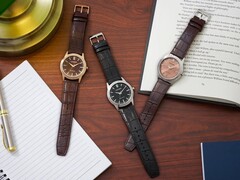 Tres relojes Citizen Rolan dispuestos sobre un escritorio de madera junto a un cuaderno, un bolígrafo, una lámpara y un libro abierto, entre los que se encuentra el modelo AW2110-14Z con esfera color salmón.