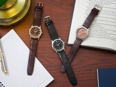 Tres relojes Citizen Rolan dispuestos sobre un escritorio de madera junto a un cuaderno, un bolígrafo, una lámpara y un libro abierto, entre los que se encuentra el modelo AW2110-14Z con esfera color salmón.