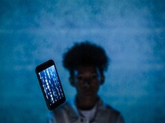 Smartphone flotante con código en la pantalla frente a un fondo azul, con una persona desenfocada detrás