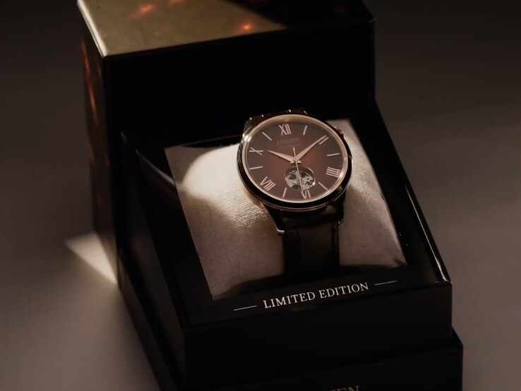 Una toma más amplia, con una iluminación dramática, del reloj Citizen colocado sobre un cojín dentro de su caja de presentación oscura y con varios niveles. Un cálido foco ilumina la esfera del reloj, y la palabra «CITIZEN» aparece impresa en el borde inferior delantero de la caja.