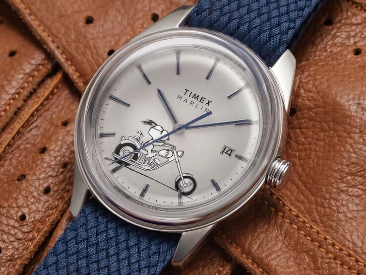 Vista frontal en ángulo del reloj Peanuts x Timex Marlin Jet Automatic Easy Rider, en la que destacan el cristal abombado, la caja de acero inoxidable en tono plateado, la esfera con motivos de Snoopy y la correa de tela azul.