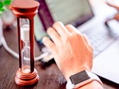 Un reloj de arena junto a una mano sobre el teclado de un ordenador portátil