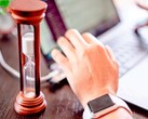 Un reloj de arena junto a una mano sobre el teclado de un ordenador portátil